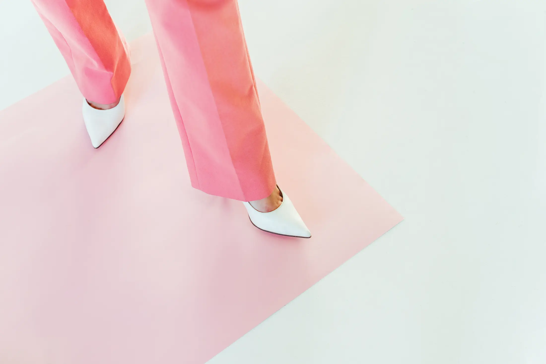 White heels and pink trousers stepping across a pink and white surface